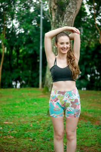 Portrait of smiling young woman exercising against trees