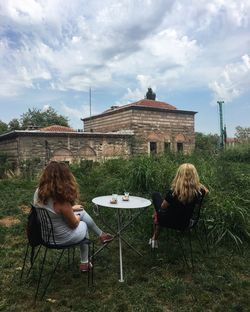 Rear view of woman sitting on chair at table against sky