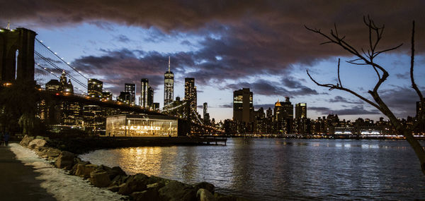 Illuminated buildings by river against sky during sunset