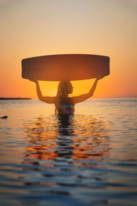 Attractive young woman in a wetsuit standing waist-deep in sea water holding a kitesurf board on her