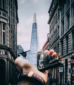 Low angle view of hand holding buildings against sky in city