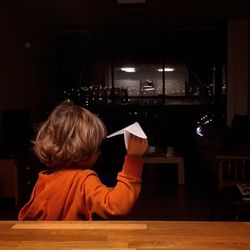 Rear view of boy playing with paper airplane at home