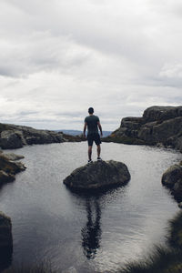 Rear view of man standing on cliff by sea against sky