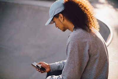 Young man text messaging on smart phone at skateboard park