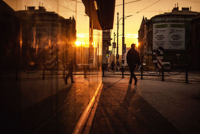 Silhouette man walking on sidewalk by building in city during sunset