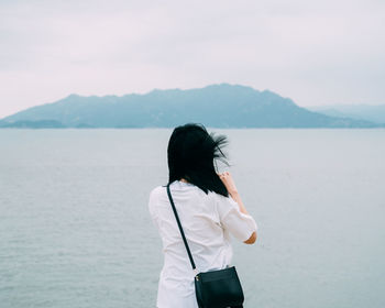 Rear view of woman standing in sea against sky