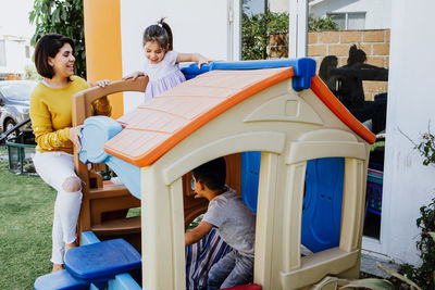 Happy latin american mother and father playing with cute little son and daughter on slides on backyard in sunlight