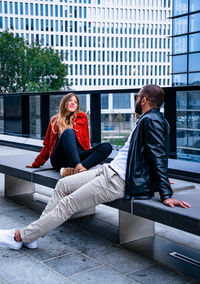 Friends sitting on seat against buildings in city