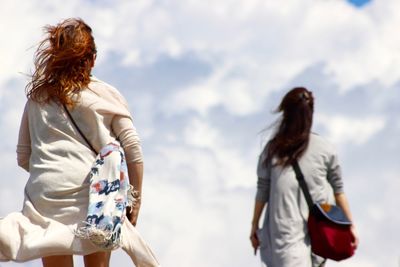 Low angle view of women against cloudy sky during sunny day