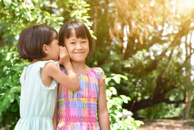 Cute girl whispering in sisters ear outdoors