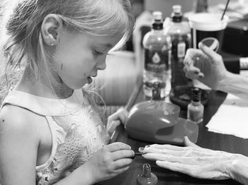 Side view of girl applying nail polish on woman hand over table
