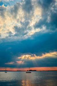 Silhouette of boats in sea against cloudy sky