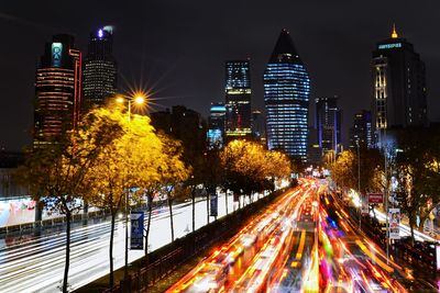 Light trails on street amidst illuminated buildings at night