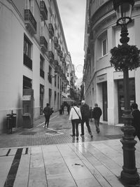 Rear view of people walking on street amidst buildings in city