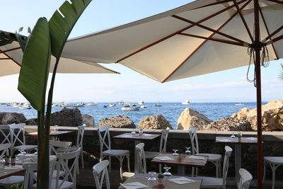 Chairs and tables at restaurant by sea against sky