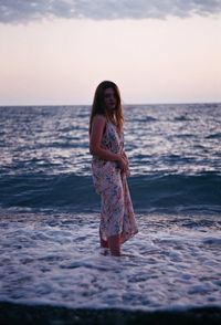 Portrait of young woman standing on beach against sky