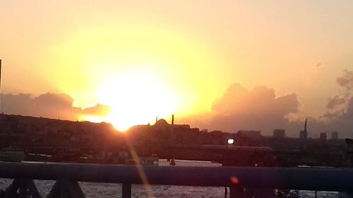 Silhouette buildings by river against sky during sunset