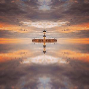 Reflection of lighthouse on sea against sky