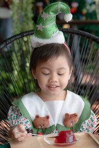 4 years old cute baby asian girl, little preschooler child wear christmas tree hat eating red jelly.