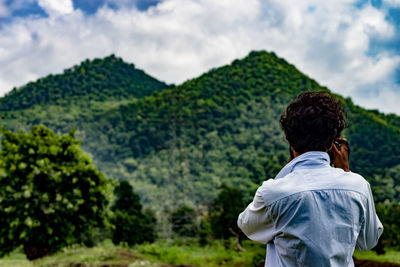 Rear view of man photographing green mountain