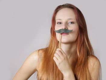 Portrait of woman holding artificial moustache against white background