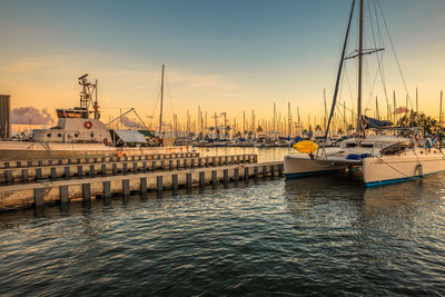 Sailboats moored on sea against sky during sunset