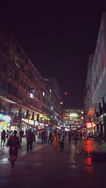 People walking on illuminated street amidst buildings in city at night