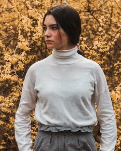 Thoughtful young woman standing against trees at park during autumn