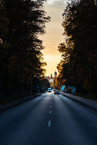 Road amidst trees against sky at sunset