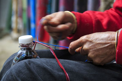 Midsection of person weaving thread with bottle