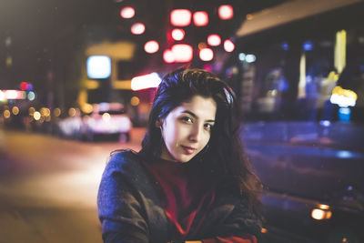 Portrait of smiling young woman standing in illuminated city at night