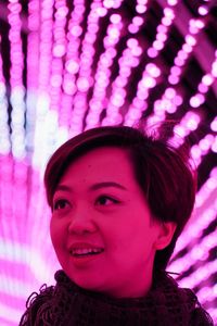 Young woman looking away against illuminated lighting equipment