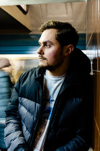 Young man looking away while standing by wall