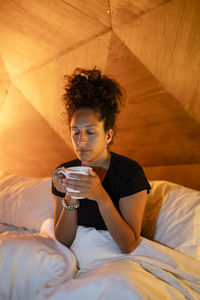 Young woman using mobile phone while sitting on bed at home