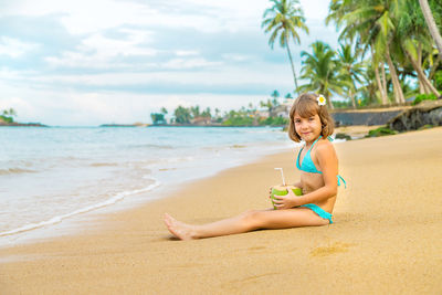 Portrait of smiling girl with coconut by seashore at beach