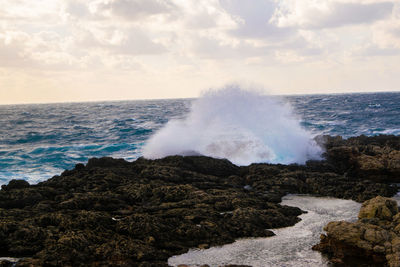 Waves splashing on rocks at shore against sky