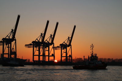 Silhouette of cranes at harbor during sunset