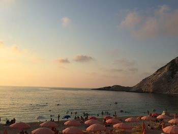 People relaxing at beach against sky during sunset