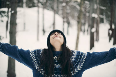 Happy woman standing with arms raised on snowy field during winter