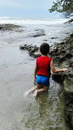 Rear view of boy by rock in sea