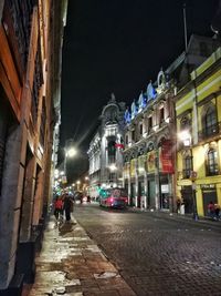 People on illuminated street amidst buildings at night