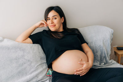 Portrait of pretty enjoying pregnant woman sitting on the sofa.