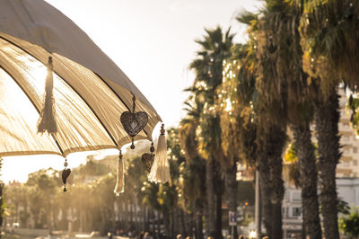 Heart shape decorations and tassels hanging on parasol against palm trees