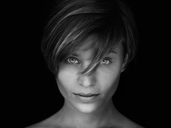 Close-up portrait of smiling young woman against black background