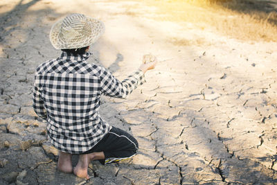 Rear view of person holding rocks while kneeling on cracked field