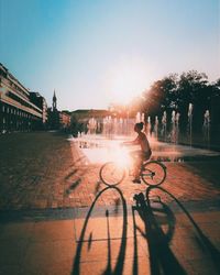 Side view of woman riding bicycle on street in city at sunset