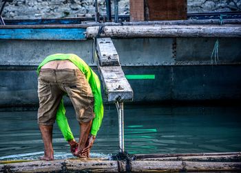 Rear view of man bending on wooden raft at lake