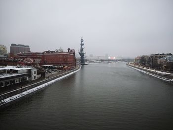 Bridge over river by buildings in city against clear sky