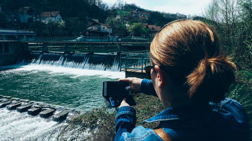 Rear view of woman photographing dam through mobile phone