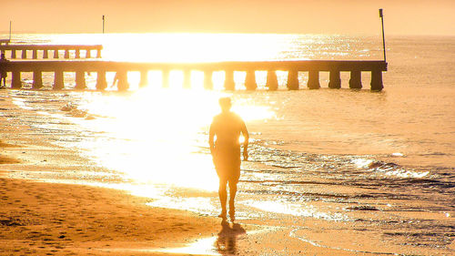 Rear view of silhouette man standing at beach during sunset